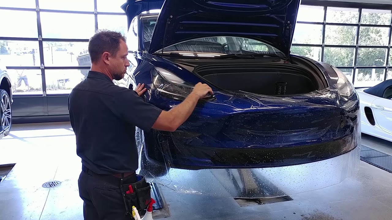 Person applying clear paint protection film to the front of a Tesla bumper.