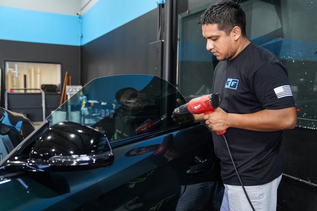 Window Tint Installer using a heating tool to shape the custom window film to the bmw window